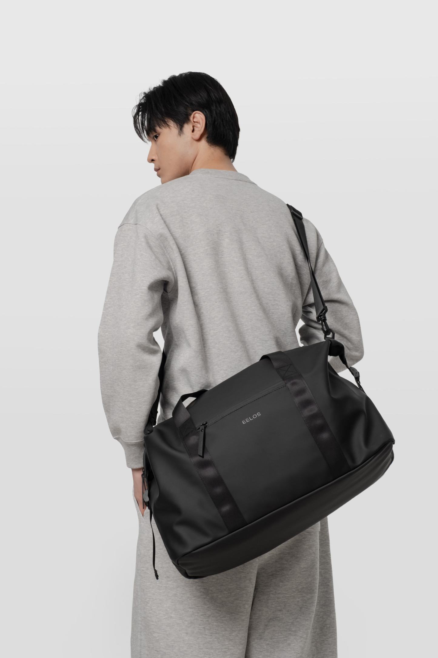Person wearing a black duffel bag on a plain background