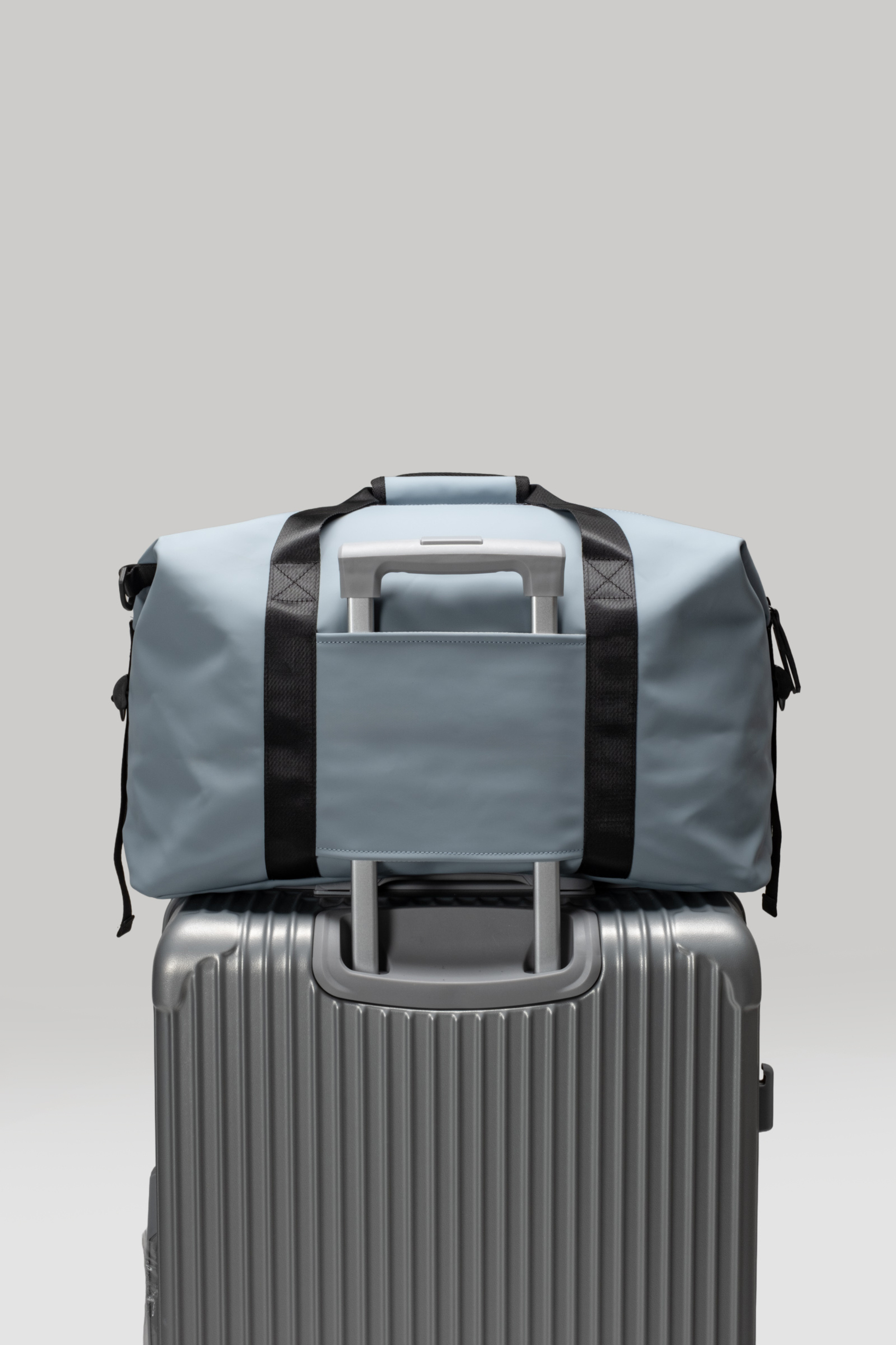 Gray duffel bag with black straps on top of a silver suitcase against a light gray background
