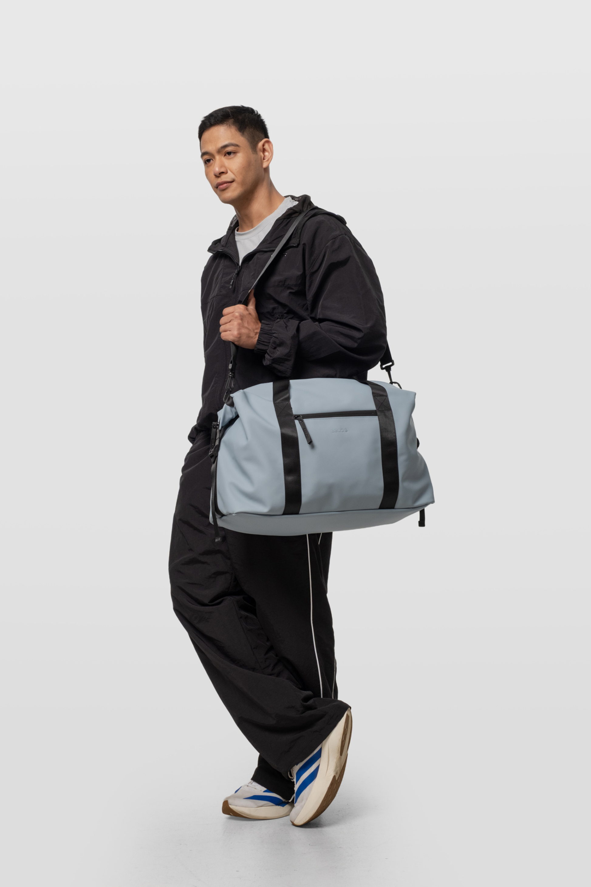 Person holding a gray duffel bag against a white background