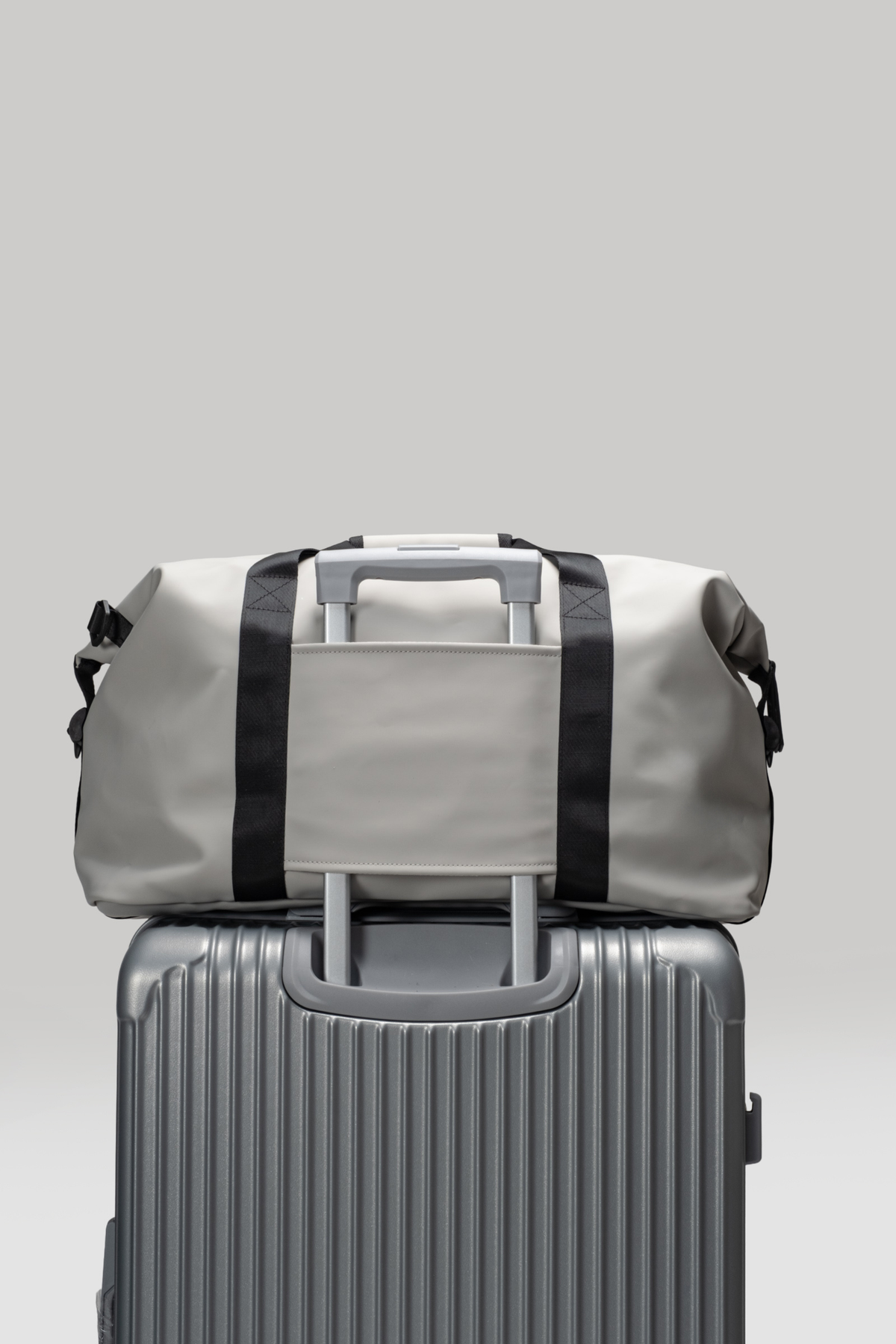 Gray duffel bag on top of a silver suitcase against a light gray background