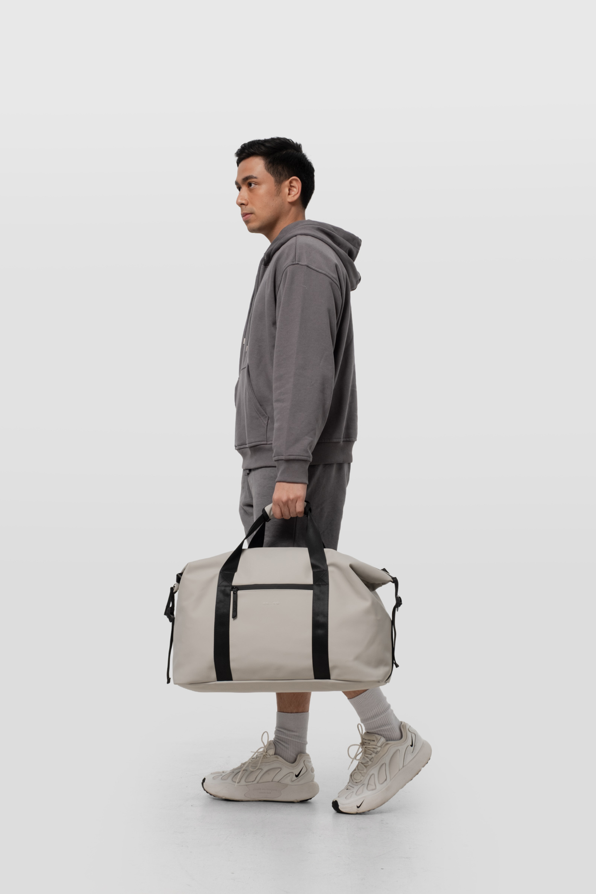 Man holding a gray duffel bag against a white background