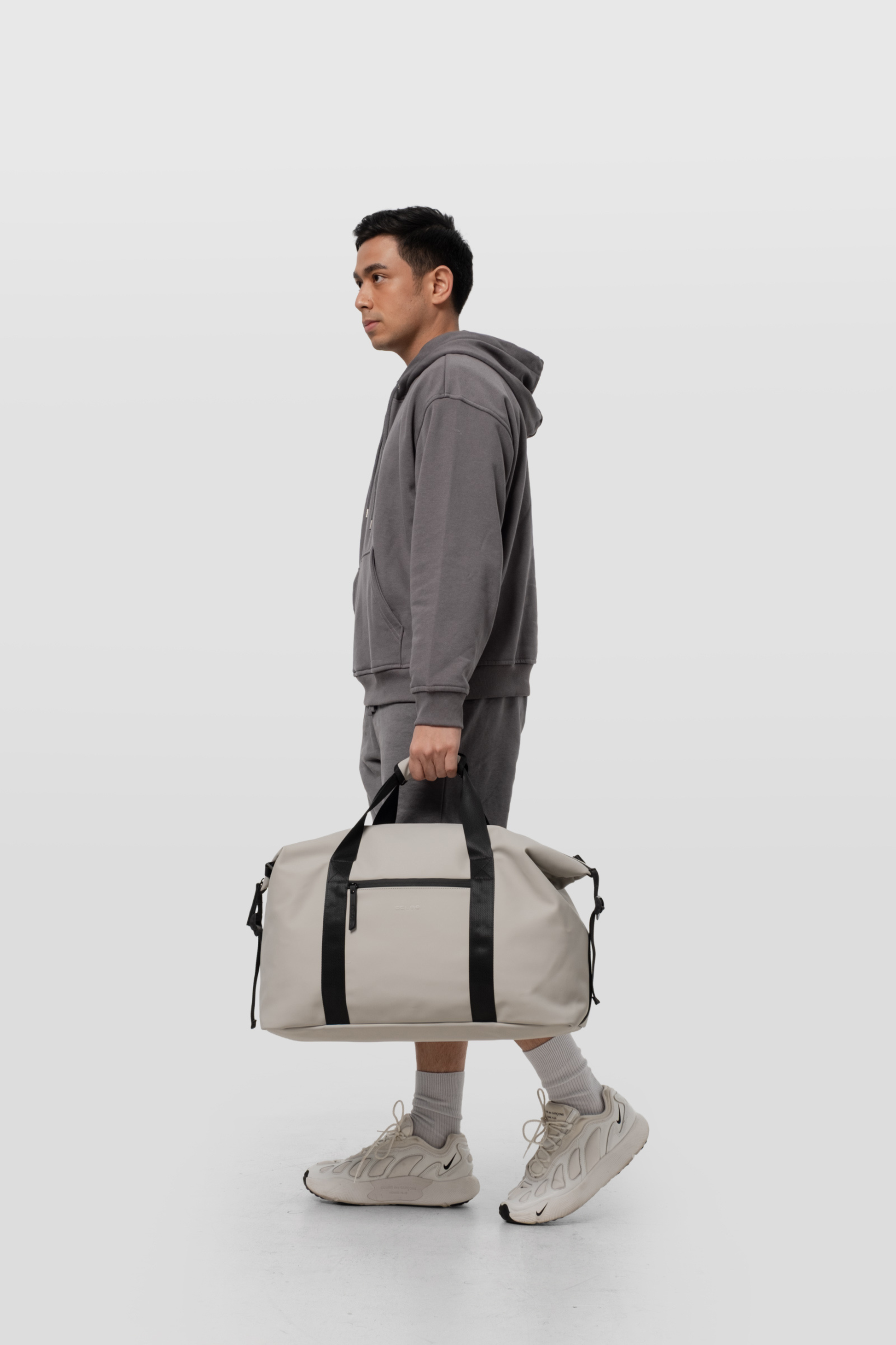 Man holding a gray duffel bag against a white background
