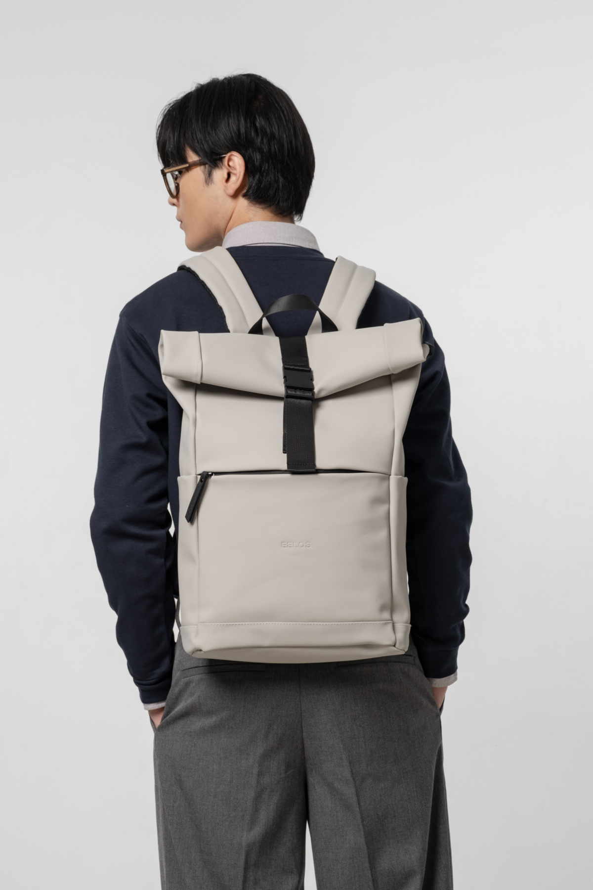 Person wearing a beige roll-top backpack on a white background