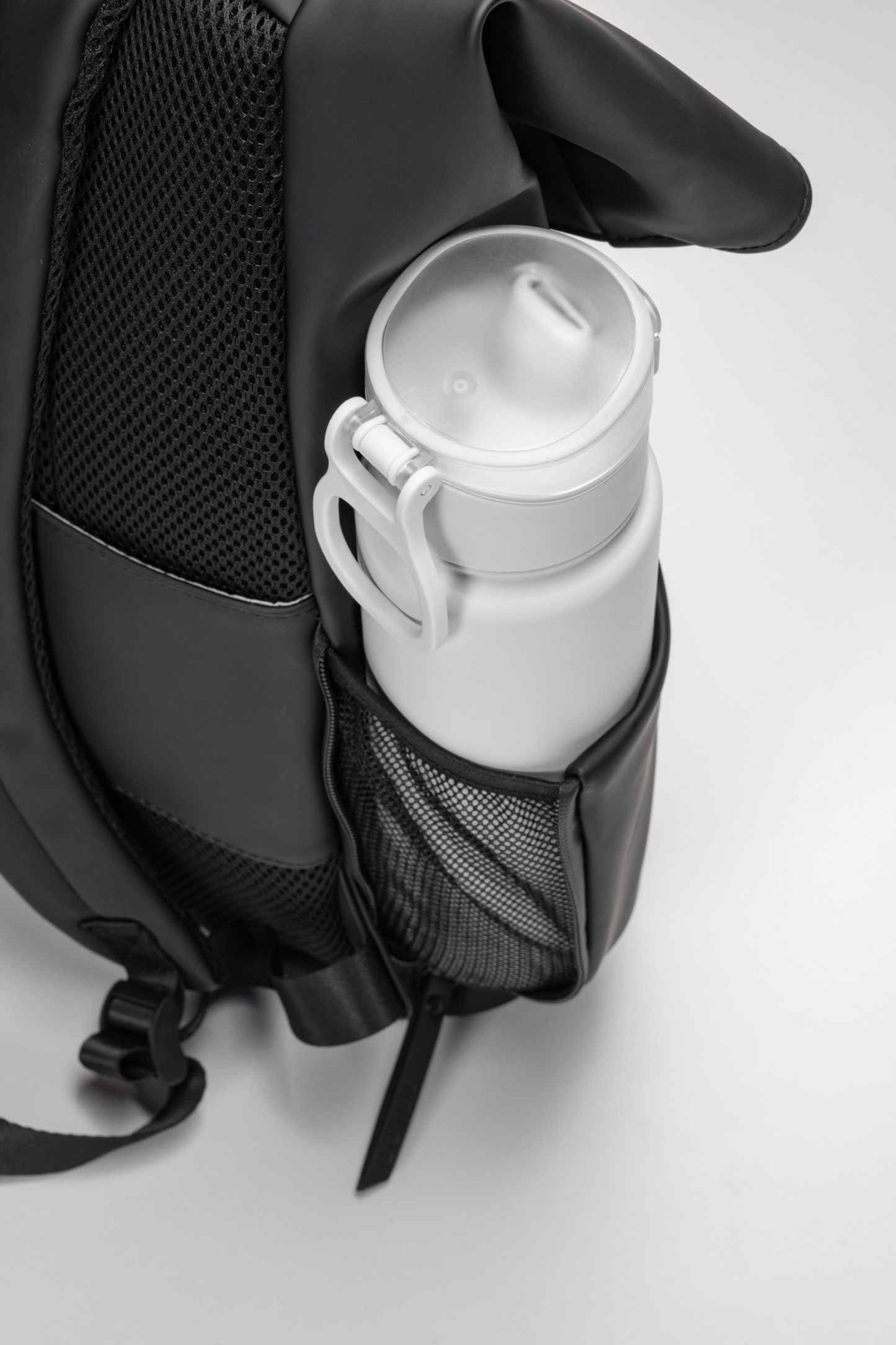 Black backpack with a white water bottle inside on a light gray background