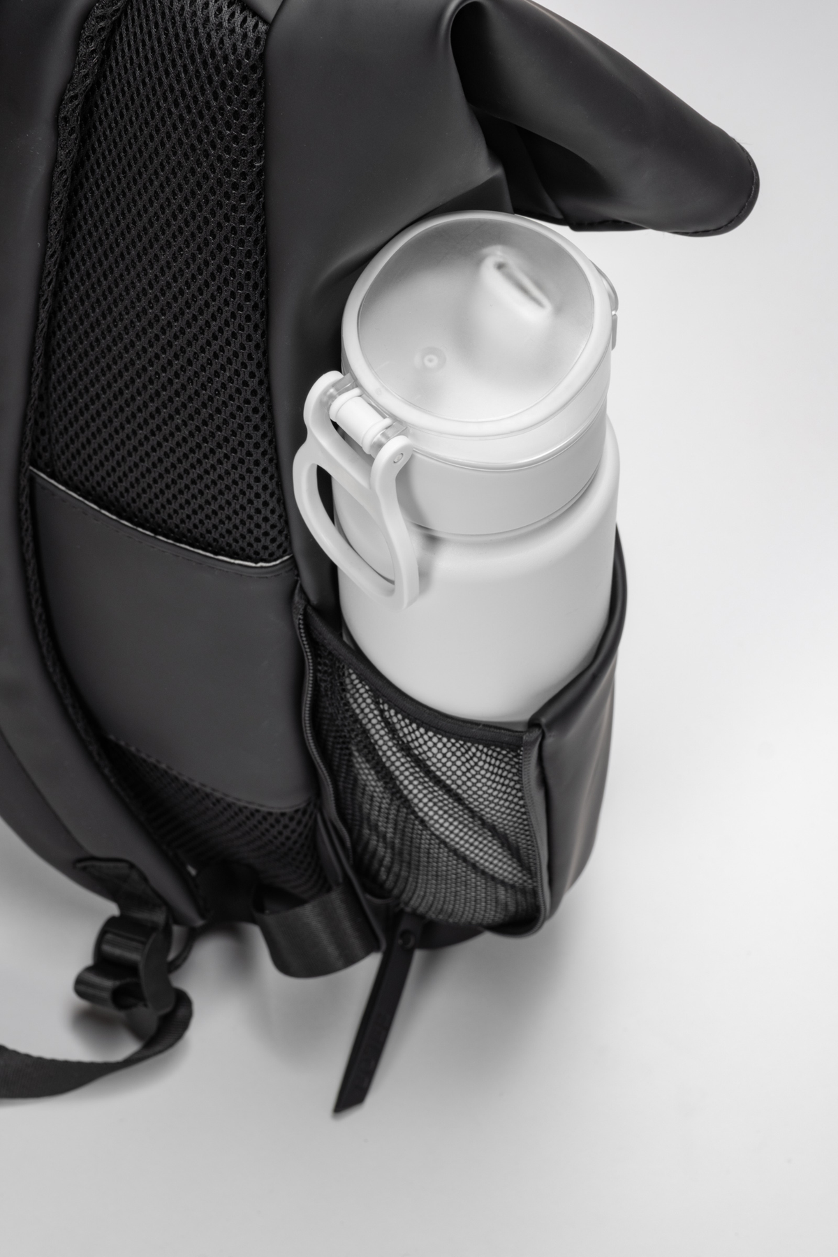 Black backpack with a white water bottle inside on a light gray background