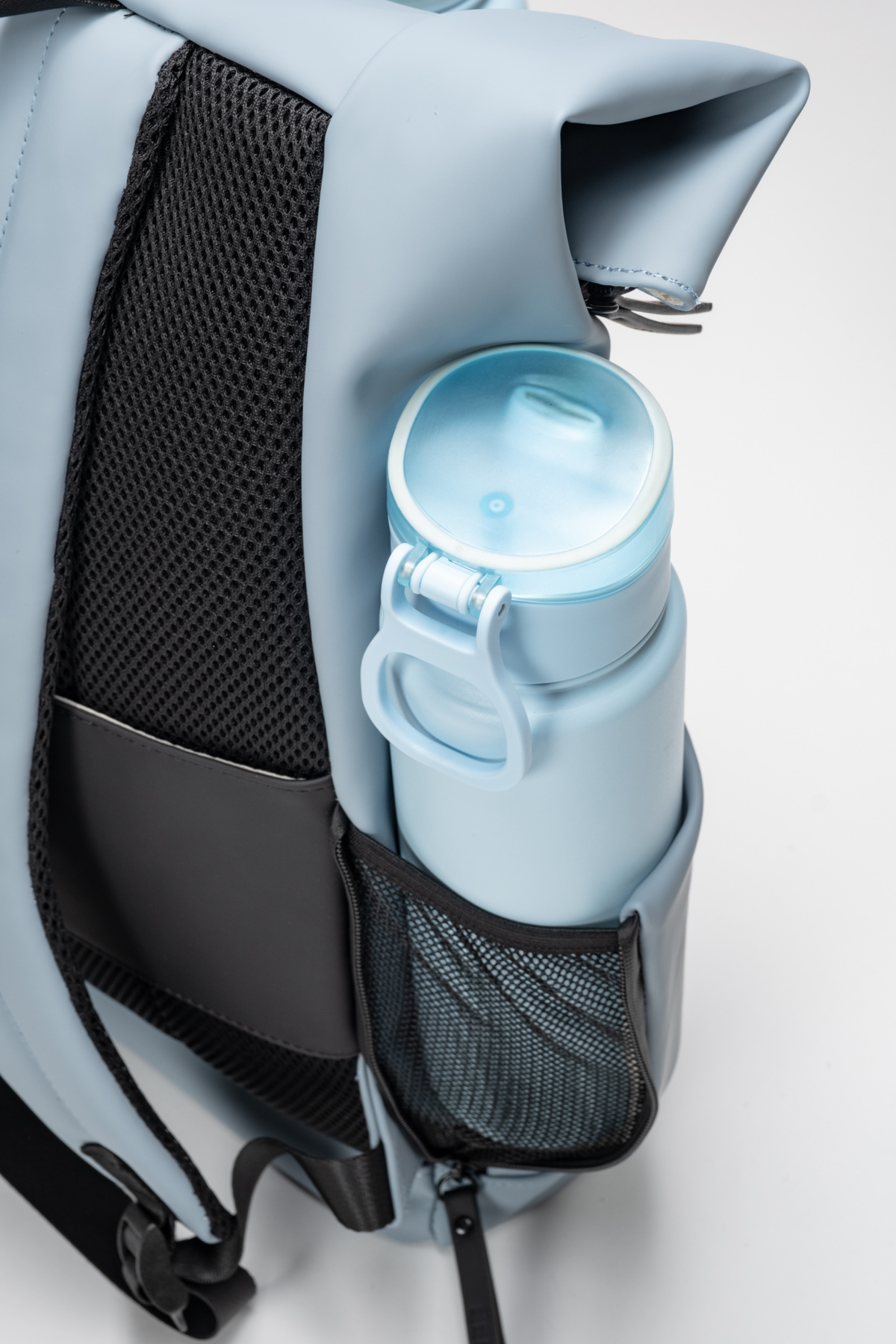 Light blue backpack with a water bottle in a black pocket on a white background